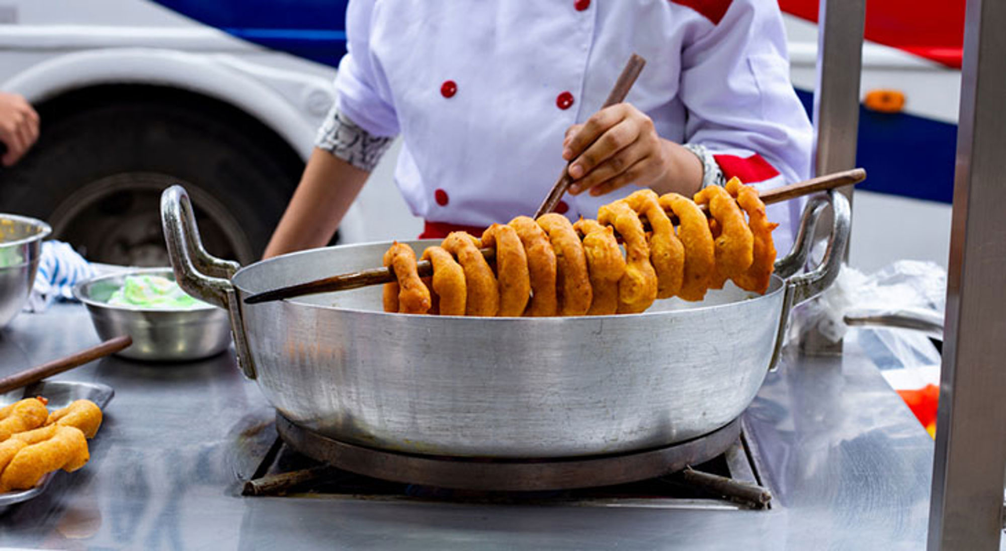 Vegetarisch Peruaans gerecht Straatkok frituurt spiraalvormige snack op een spies in een grote pan met olie.