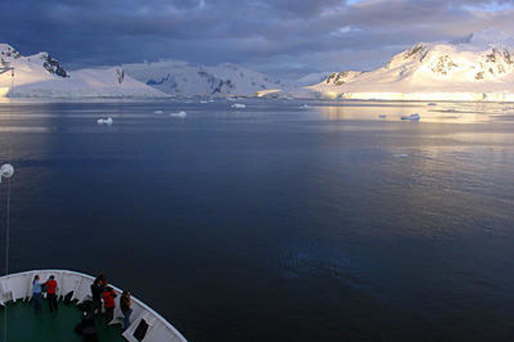Expeditiecruise in Antarctica met uitzicht op ijsbergen en besneeuwde bergen voorbij de Zuidpoolcirkel.