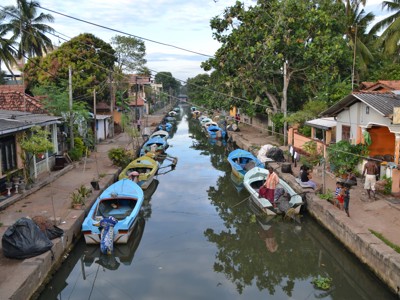Kanaal met aangemeerde bootjes langs huizen en palmbomen in Sri Lanka.