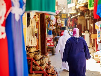 Drukke souk in Marokko met kleurrijke kramen en mensen die door een smalle straat lopen.