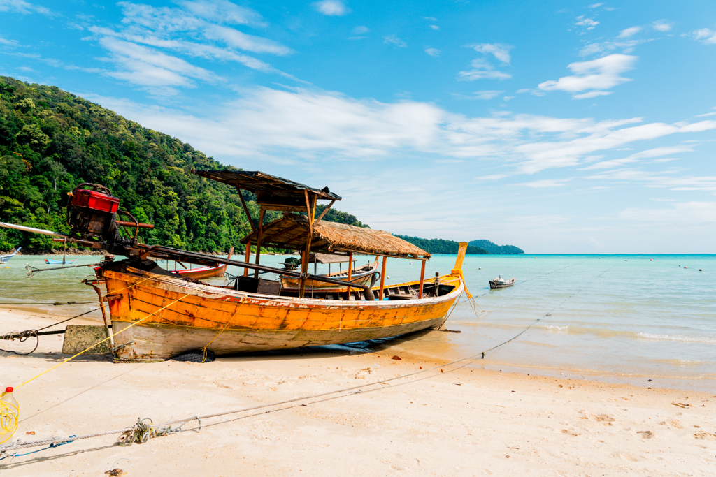 Longtailboot op een zandstrand in Thailand met turquoise zee en groene jungle op de achtergrond.
