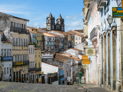 Straat in Salvador de Bahia met kleurrijke koloniale gevels en een kerk met twee torens in de verte.