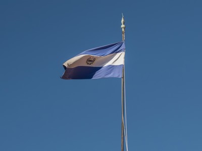 Vlag van El Salvador wappert aan een vlaggenmast tegen een heldere blauwe lucht.