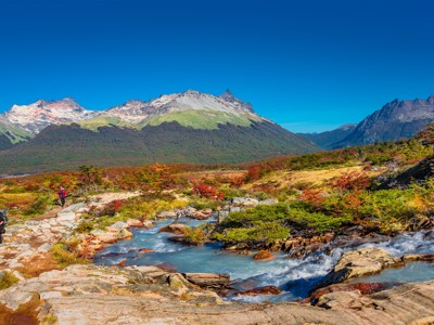 Wandelaars langs een rivier met uitzicht op bergtoppen in Patagonië.