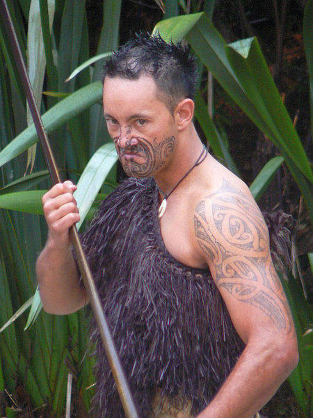 Maori-man met traditionele tatoeages en speer tijdens culturele voorstelling in Nieuw-Zeeland.