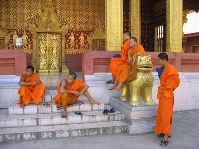 Boeddhistische monniken in oranje gewaden bij de gouden tempelingang in Laos, Route Laos & Cambodja.