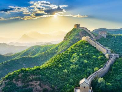 De Chinese Muur slingert over groene bergen bij zonsopkomst, tijdens een groepsrondreis China.