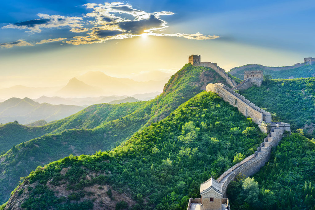 De Chinese Muur slingert over groene bergen bij zonsopkomst, tijdens een groepsrondreis China.