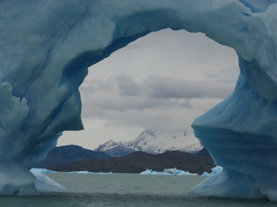 Blauwe ijsboog bij een gletsjermeer in Patagonië, met besneeuwde bergen op de achtergrond.