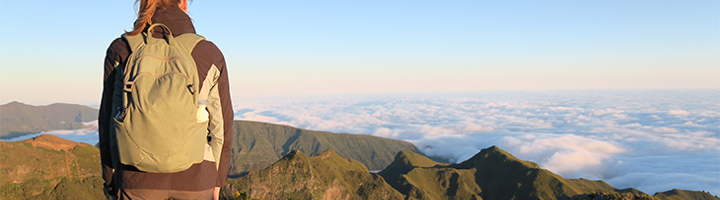 Wandelaar met rugzak kijkt uit over berglandschap en wolkendek op Madeira.