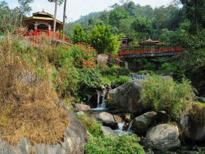 Rode bruggen en paviljoens bij een beek met kleine waterval in een groene vallei in Sikkim.