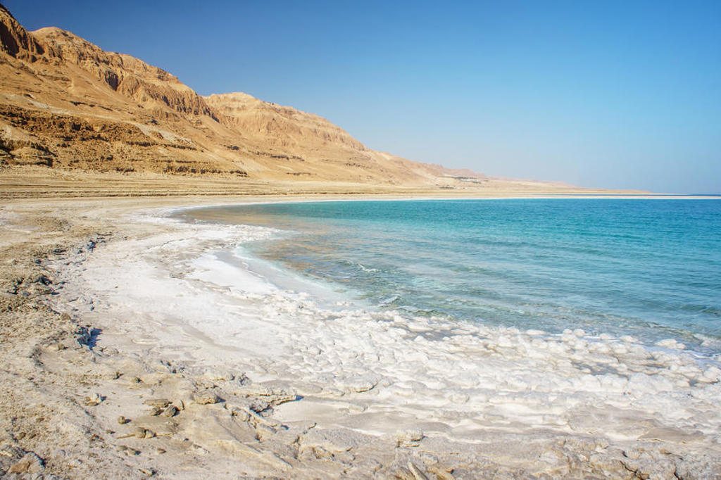 Zoutkristallen aan de oever van de Dode Zee met woestijnbergen op de achtergrond, Israël en Jordanië.