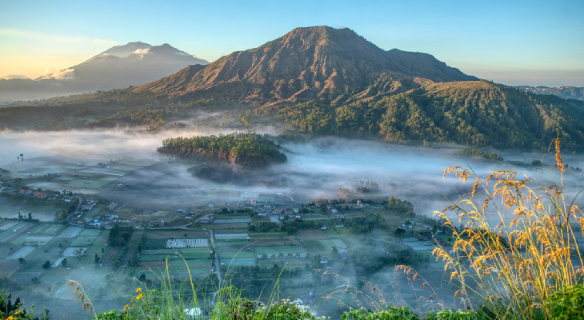 Mount Batur op Bali Zonsopgang boven een berglandschap met mist in de vallei en groene akkers op de voorgrond.