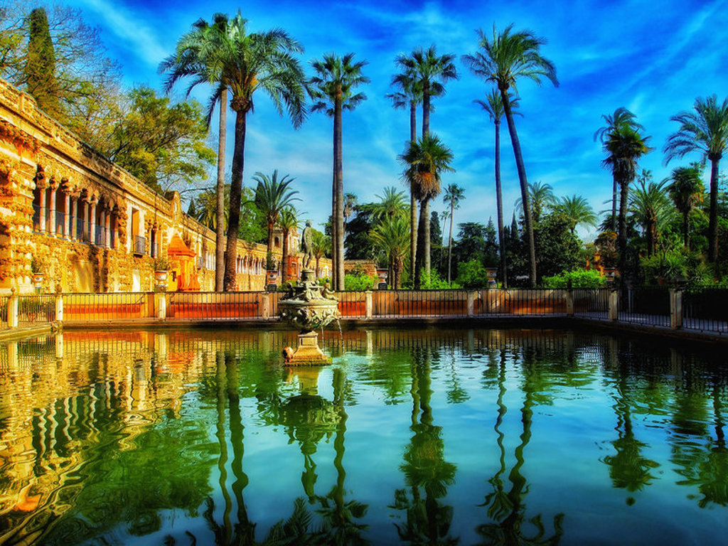 Paleis en palmbomen weerspiegeld in een vijver in het Alcázar van Sevilla tijdens een familiereis Spanje & Portugal.