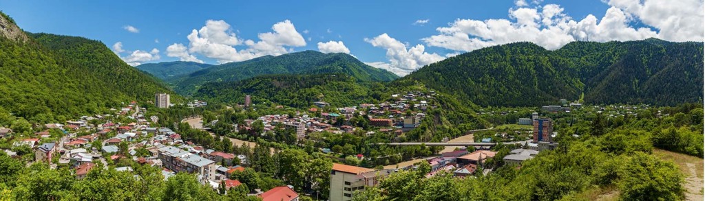 Panorama van een Georgisch bergdorp in een groene vallei, omringd door beboste bergen onder een blauwe lucht.
