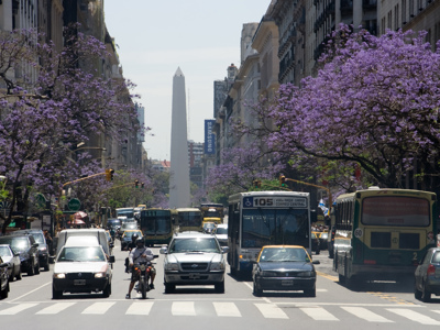 Drukke Avenida 9 de Julio in Buenos Aires met jacarandabomen en de Obelisco op de achtergrond.