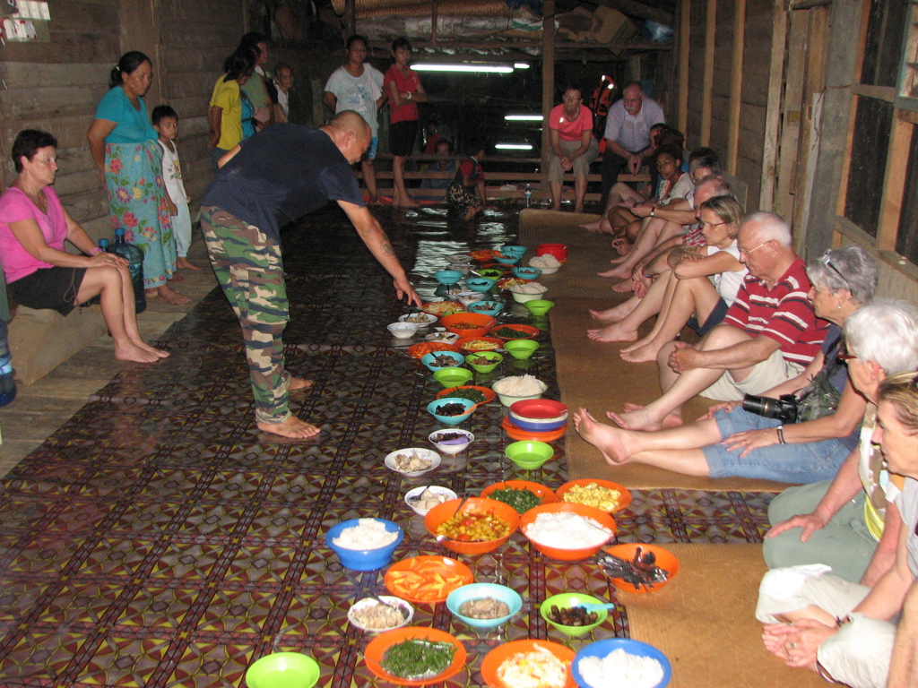 Groepsmaaltijd in een longhouse tijdens rondreis door Maleisisch Borneo, met schalen eten op matten.
