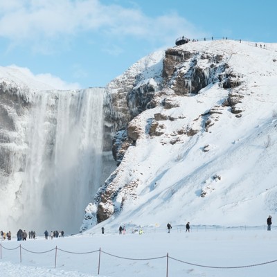 Skógafoss-waterval in de winter, met besneeuwde kliffen en bezoekers in IJsland.