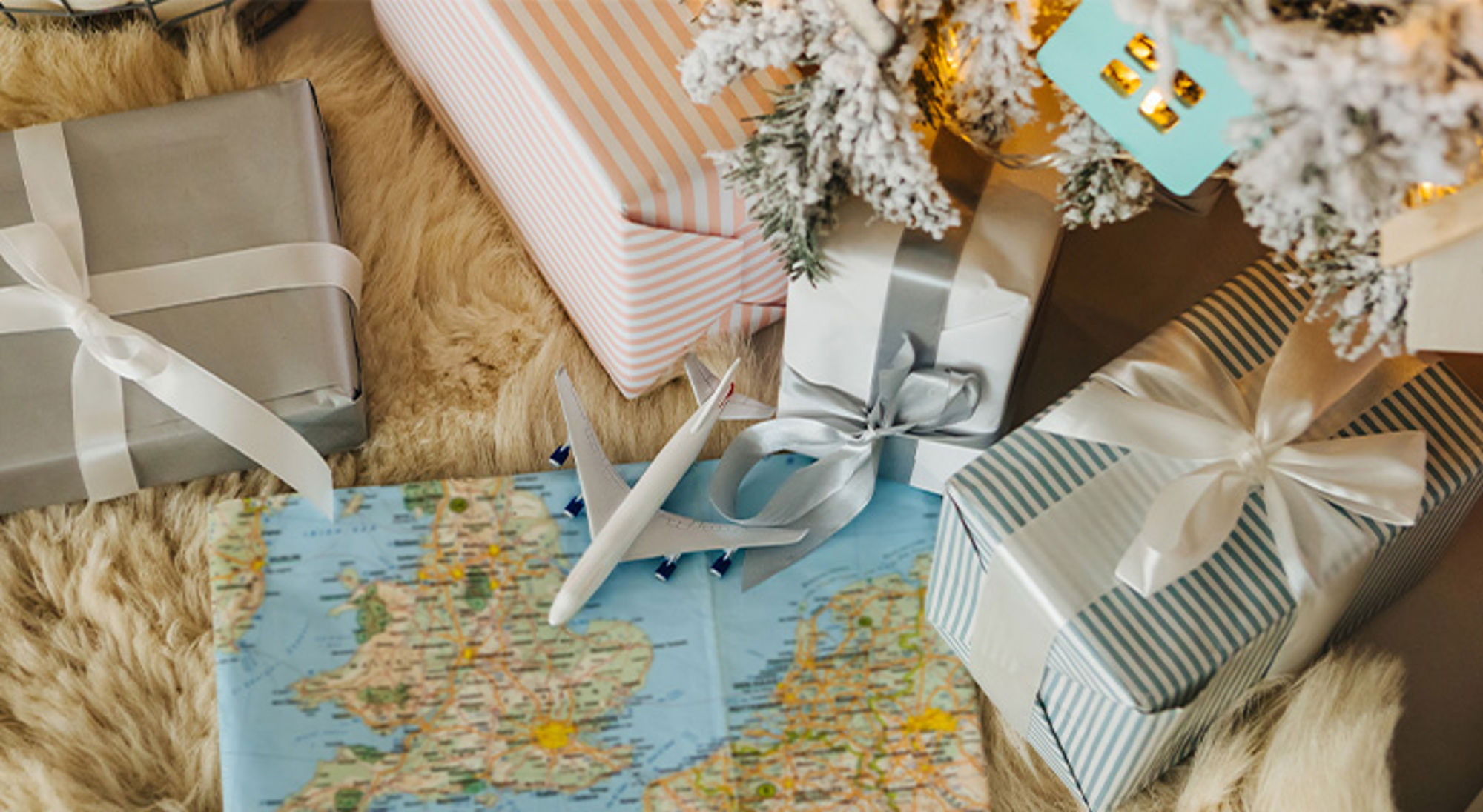 Kerstcadeaus Ingepakte cadeaus met strik naast een vliegtuigje op een landkaart, als inspiratie voor een reis cadeau.