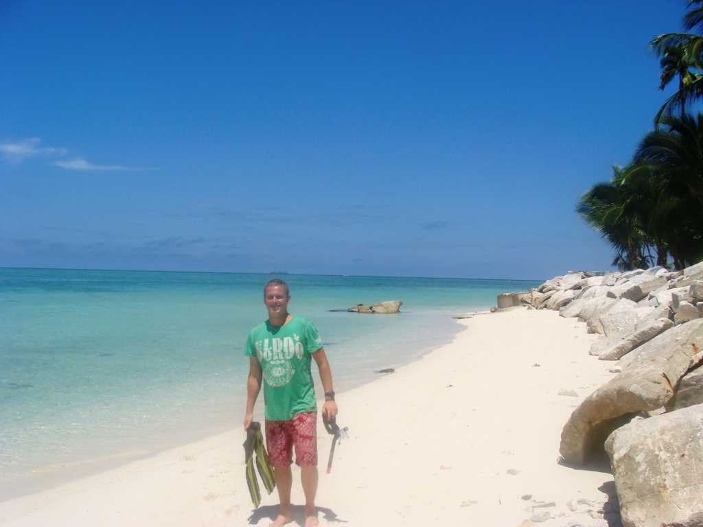 Man met snorkelspullen op wit zandstrand met palmen en turquoise zee tijdens rondreis Maleisisch Borneo.