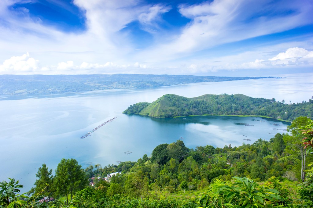 Uitzicht over het Tobameer op Sumatra met groen schiereiland en helderblauwe lucht.