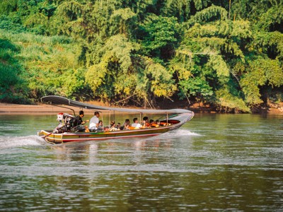 Longtailboot met reizigers op de rivier langs groene jungle in Thailand.