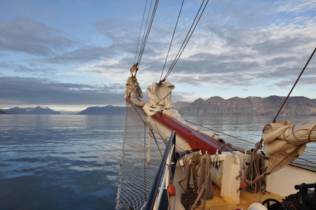 Zeilschip de Antigua vaart langs de kust van Spitsbergen met bergen op de achtergrond.