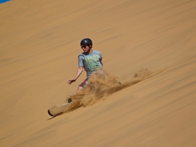 Sandboarden van een zandduin in Namibië, met opspattend zand.