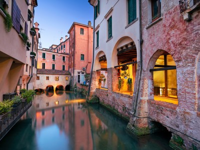 Avondzicht op een smal kanaal met historische gevels en bogen in Treviso, Italië.