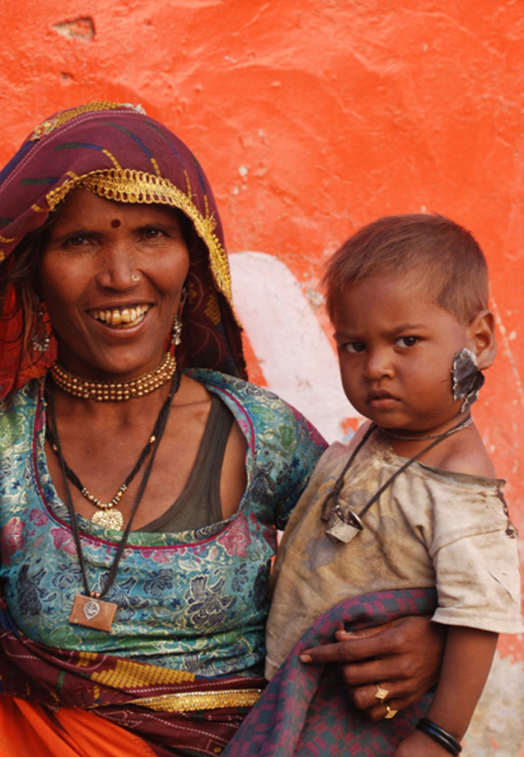Portret van vrouw in traditionele kleding met kind in Gujarat, India, tegen een oranje muur.