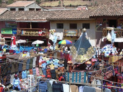 Drukke markt in Peru met kleurrijke textielkramen en religieuze processiebeelden op het plein.