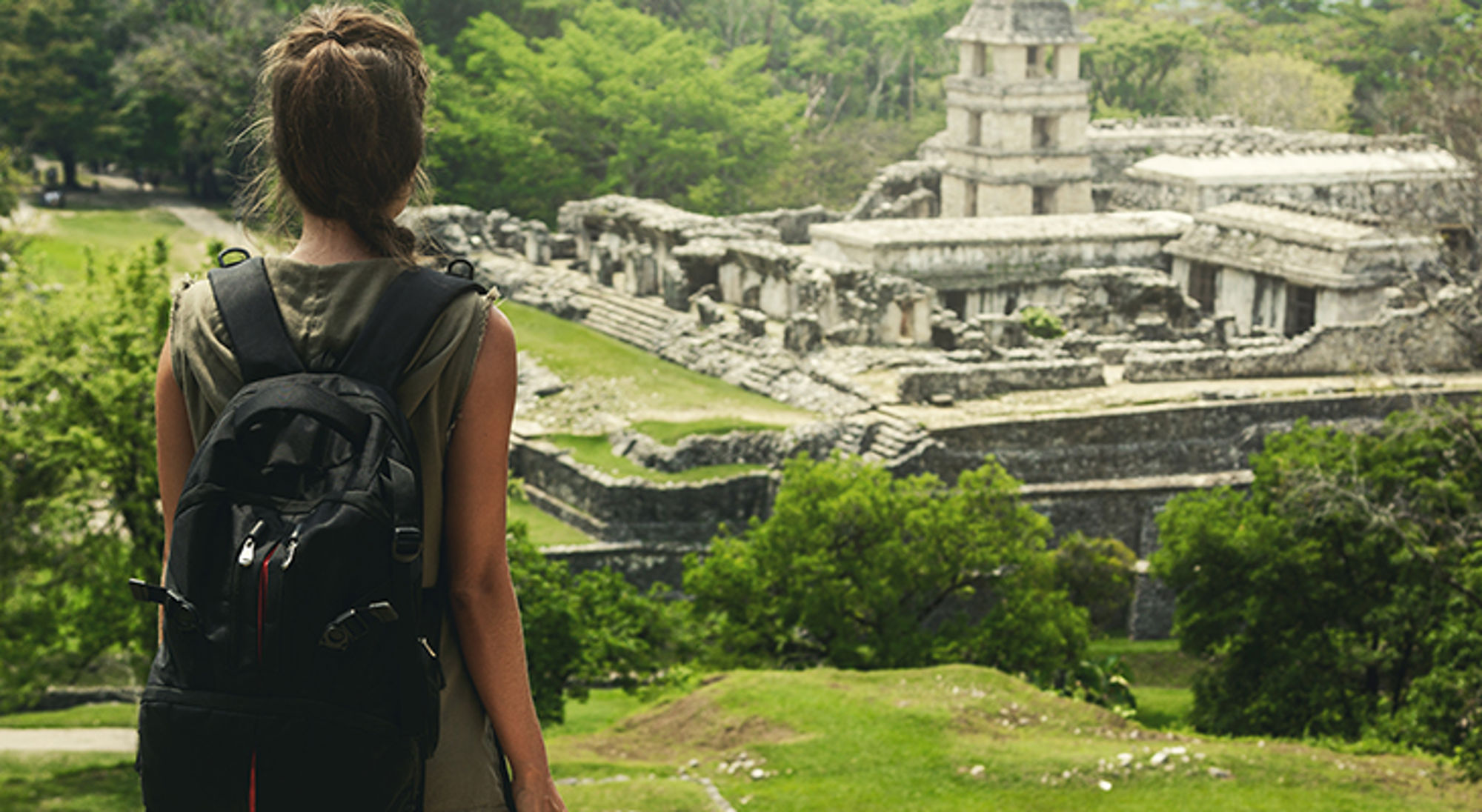 Palenque Rugzaktoerist kijkt uit over de Maya-ruïnes van Palenque, omringd door tropisch groen.