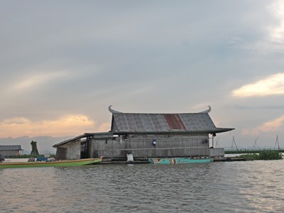Drijvend houten huis met bootjes op een meer in Sulawesi tijdens zonsondergang.