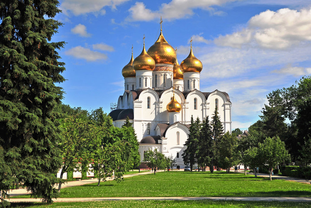 Witte orthodoxe kathedraal met gouden koepels in Rusland, omringd door groen en blauwe lucht.