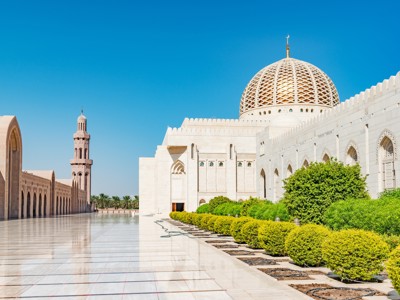Witte Sultan Qaboos Grand Mosque in Muscat, Oman, met koepel en minaret onder een blauwe lucht.