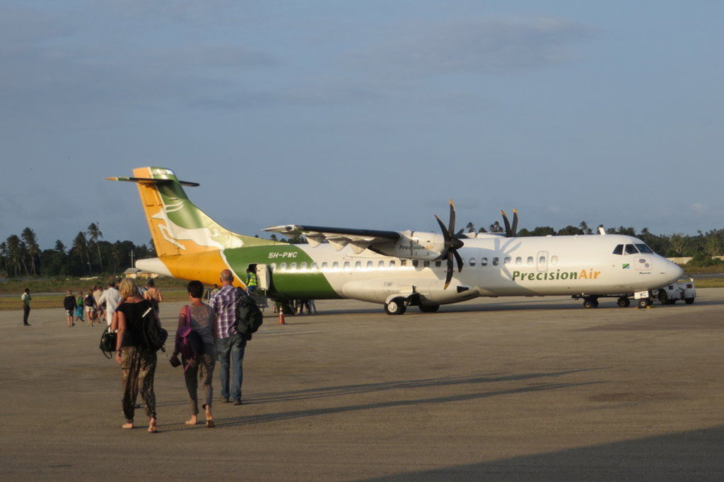 Reizigers lopen over het platform naar een Precision Air-propellervliegtuig tijdens de groepsrondreis Kenia, Tanzania en Zanzibar.