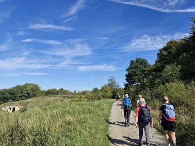 Wandelaars met rugzakken op een onverharde route van de Dutch Mountain Trail onder een blauwe lucht.