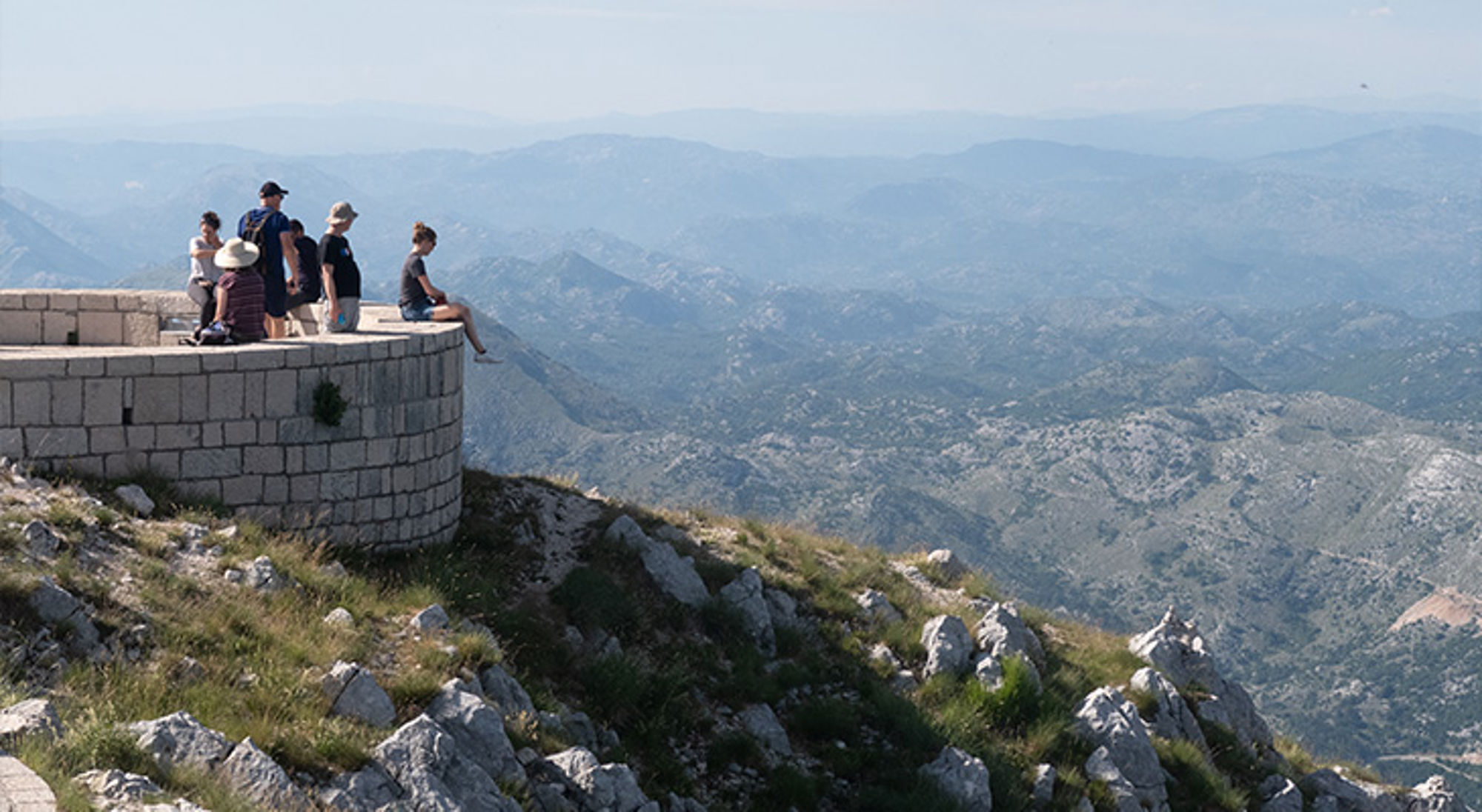 Toeristen op een uitzichtpunt op een bergtop met panoramisch uitzicht over een berglandschap.
