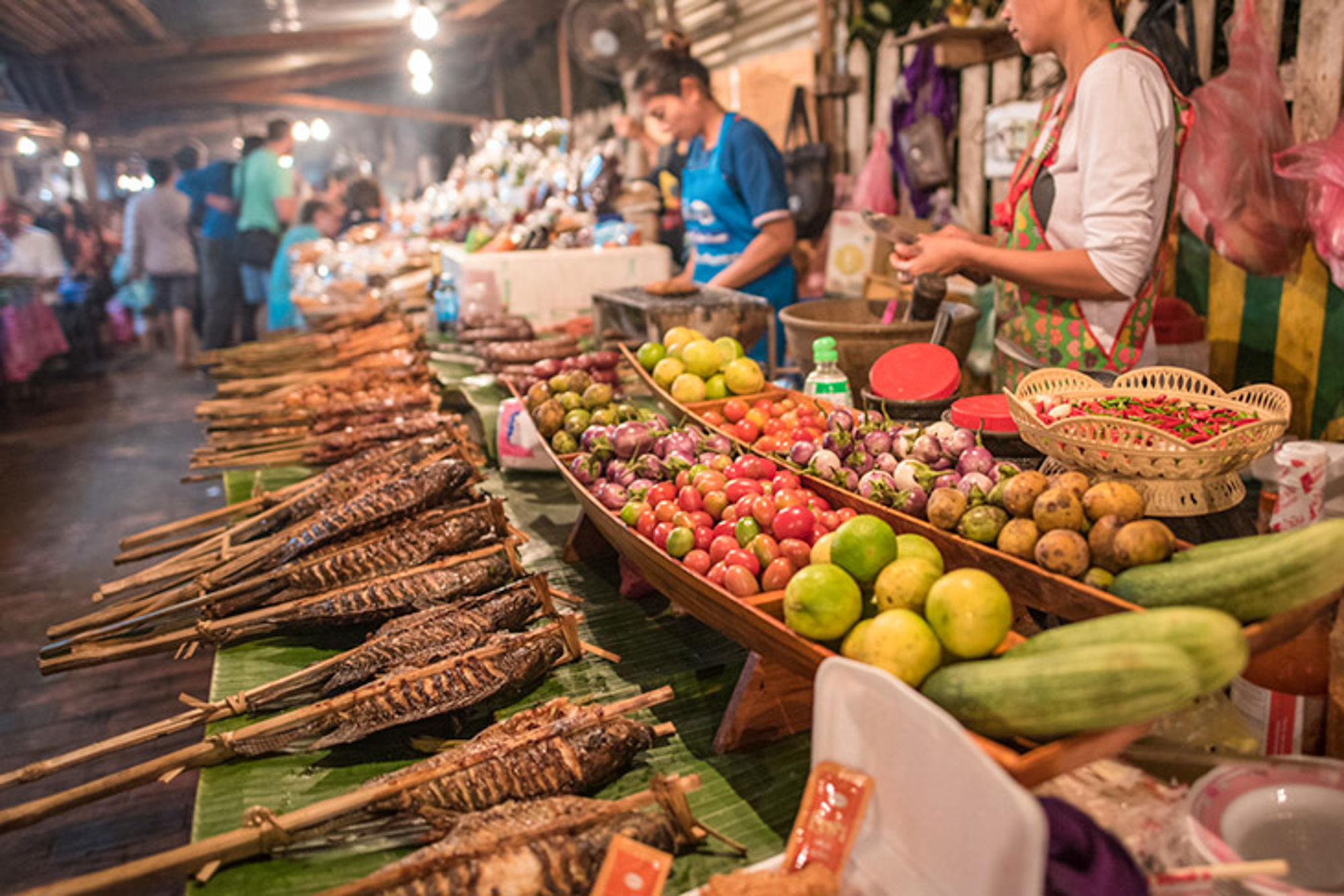 Markt in Laos Marktkraam met gegrilde vis op stokjes, verse groenten en fruit op een drukke avondmarkt.