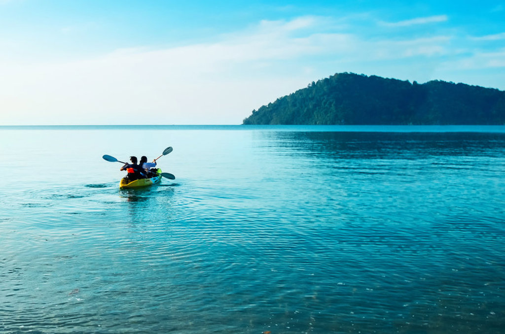 22-35ers kajakken op helderblauw water bij een groen eiland tijdens de reis Thailand, Laos en Cambodja.