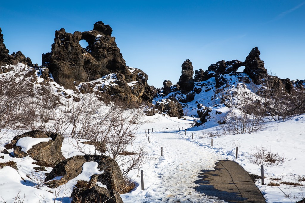 Sneeuwpad langs lavavelden en basaltrotsen in Noord-IJsland onder een heldere blauwe lucht.