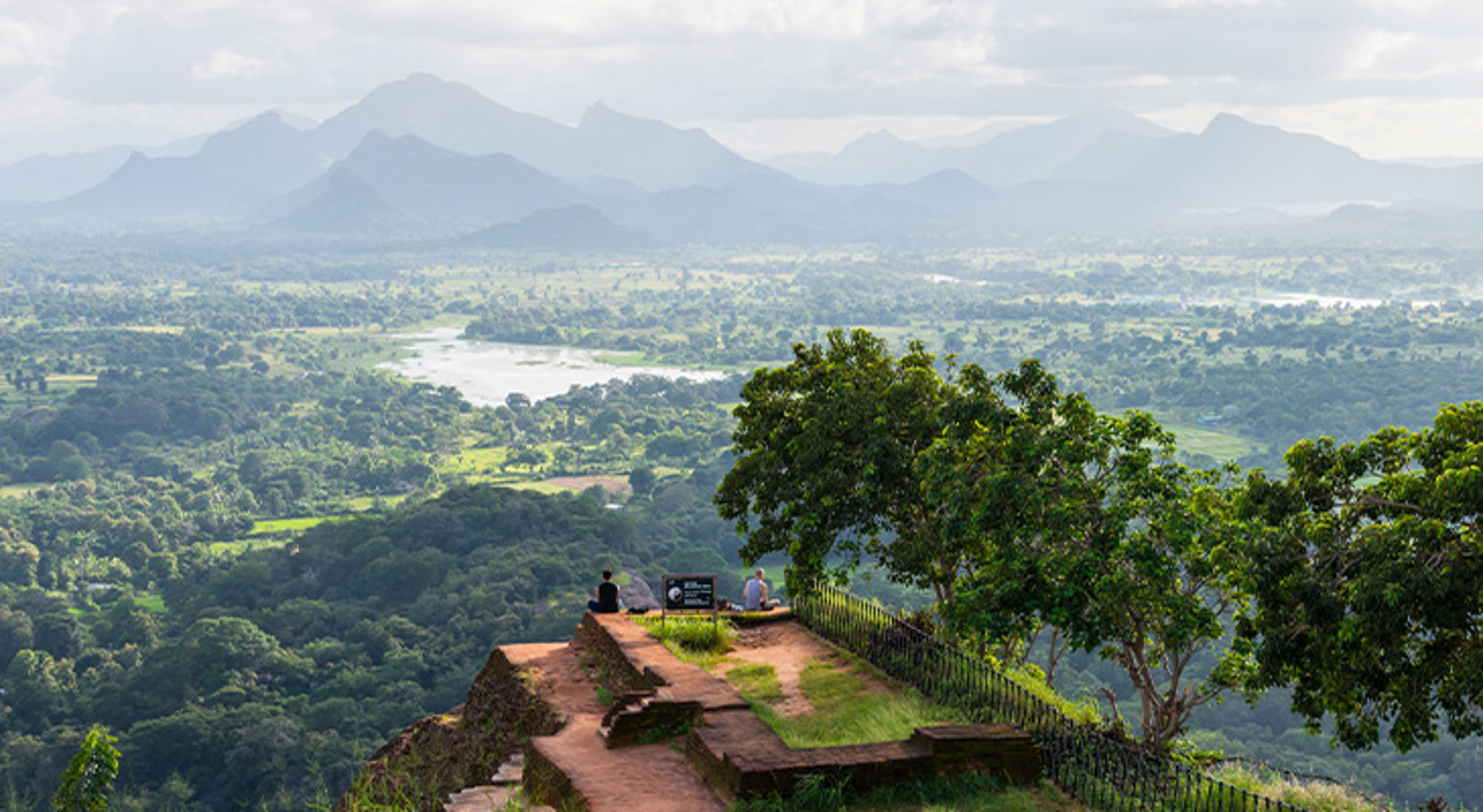 Leeuwenrots Sri Lanka Uitzicht vanaf een rotsachtig uitkijkpunt over een groene vallei met rivier en bergen op de achtergrond.