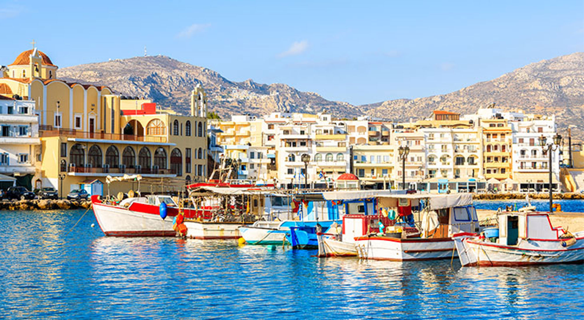 Karpathos Kleurrijke vissersboten in de haven met de stad en bergen op de achtergrond.