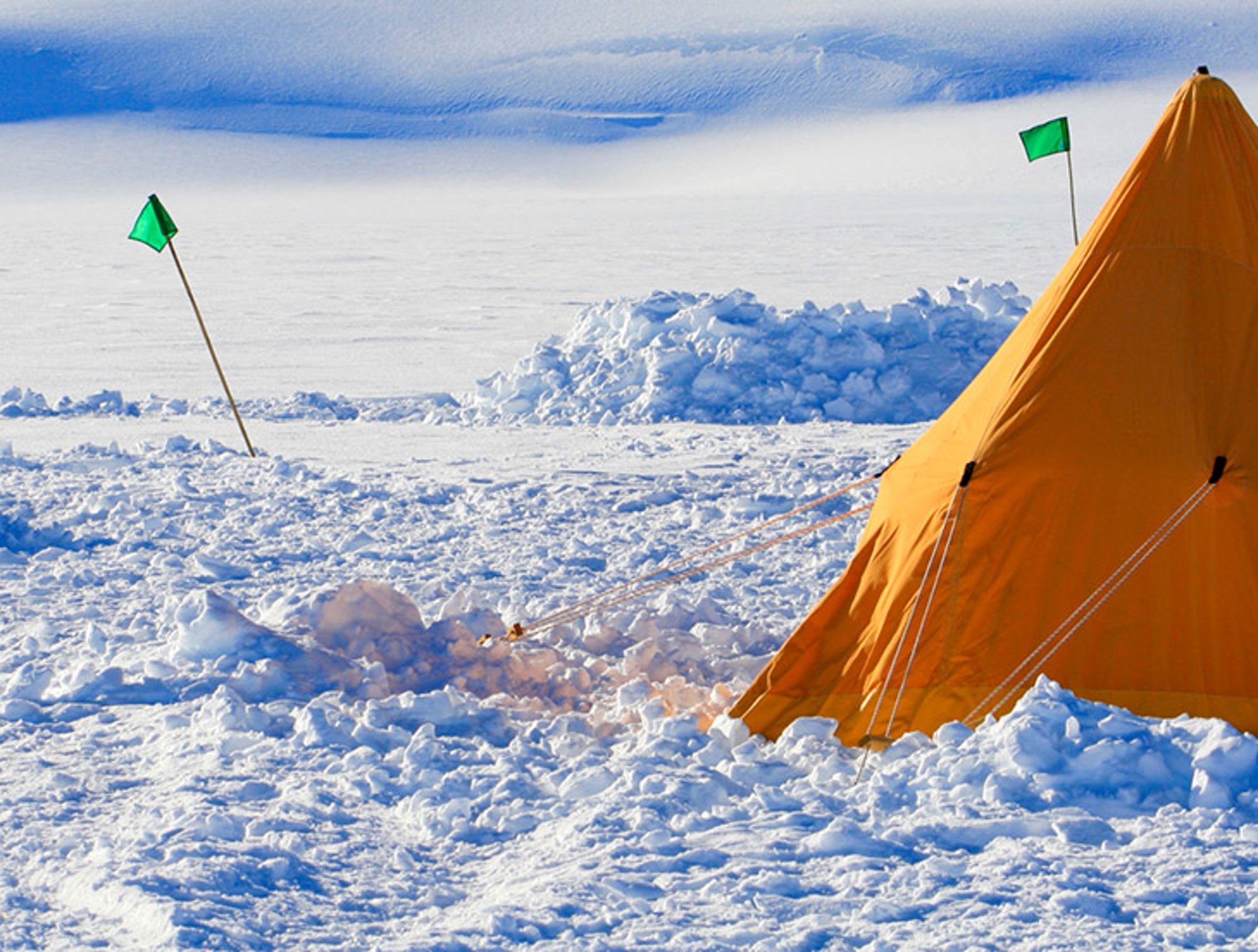 Kamperen op het ijs in Antarctica Oranje expeditietent op een besneeuwde ijsvlakte met groene vlaggen.