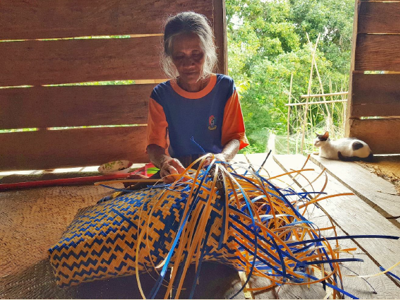 Vrouw weeft een kleurrijke mand van riet in een houten huis op Borneo.