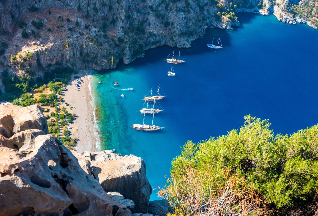 Uitzicht op een baai met turquoise zee, strand en zeilboten aan de Turquoise Kust in Turkije.