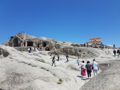 Bezoekers wandelen bij de rotswoningen van Uplistsikhe in Georgië, met een kerk op de heuvel.