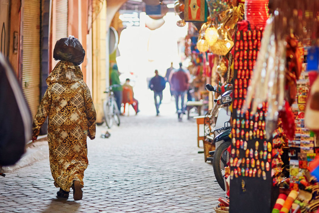 Straatbeeld in een Marokkaanse medina met kleurrijke marktkraampjes en een wandelaar in traditionele kleding.