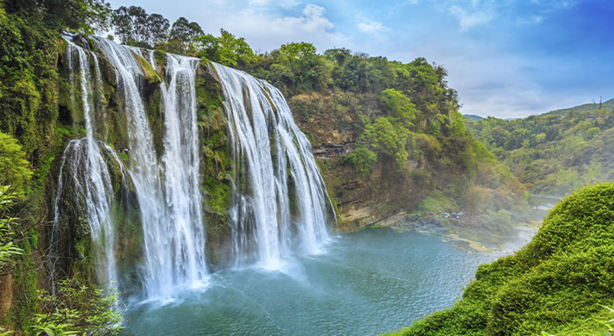 Huangguoshu waterval China Brede waterval die in een turquoise rivier stort, omringd door groen begroeide kliffen en bos.
