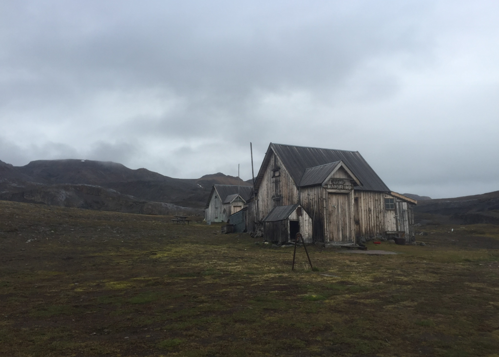 Houten gebouwen bij Camp Mansfield in het ruige landschap van Spitsbergen onder een bewolkte lucht.